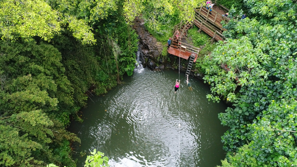 Guest ziplining over a natural swimming hole surrounded by lush greenery on Kauaʻi