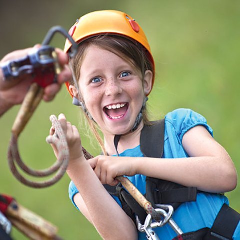 Child riding a zipline at Outfitters Kauaʻi and looking excited during a Kauaʻi adventure tour.
