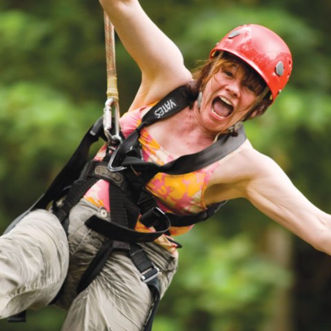 Woman smiling while ziplining on the Nui Kauaʻi Zipline tour at Kipu Ranch.