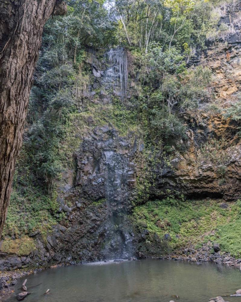 Secret Falls (Uluwehi Falls) on the Wailua River in Kauai, surrounded by lush jungle cliffs and a calm pool at the base, viewed during a guided kayaking and hiking tour.