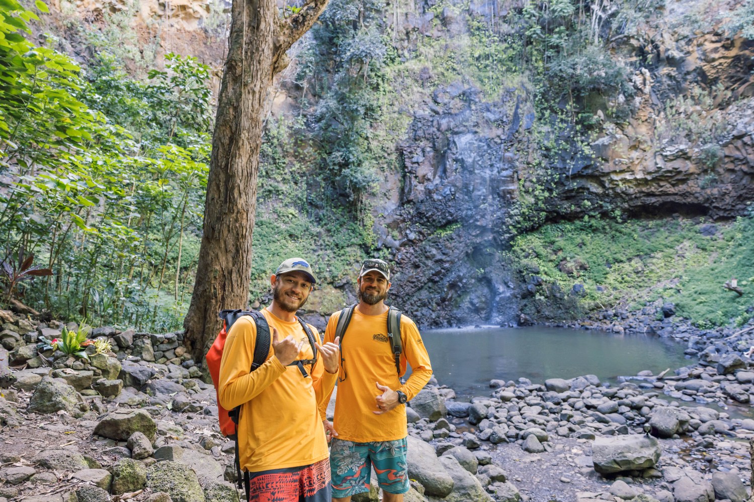 Two Outfitters Kauai guides standing in front of a waterfall, showcasing expert leadership on Kauai zipline and kayaking tours.