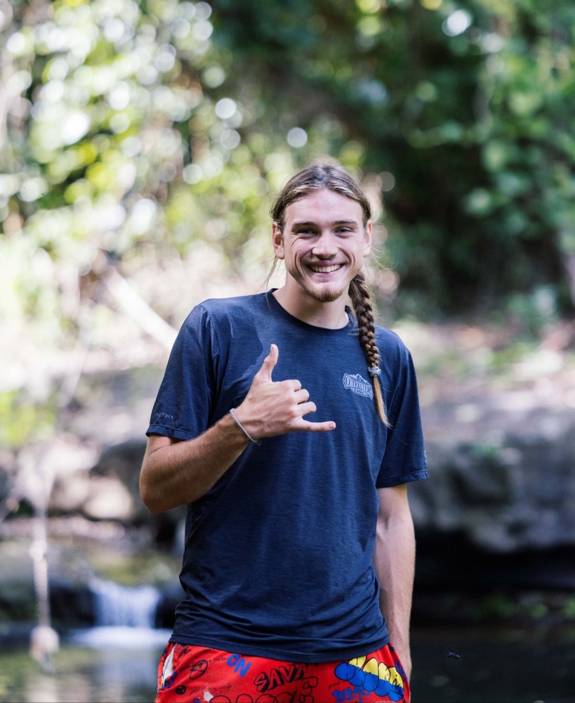 Outfitters Kauai guide smiling and throwing a shaka near a waterfall on the Zipline Safari and Huleia River adventure
