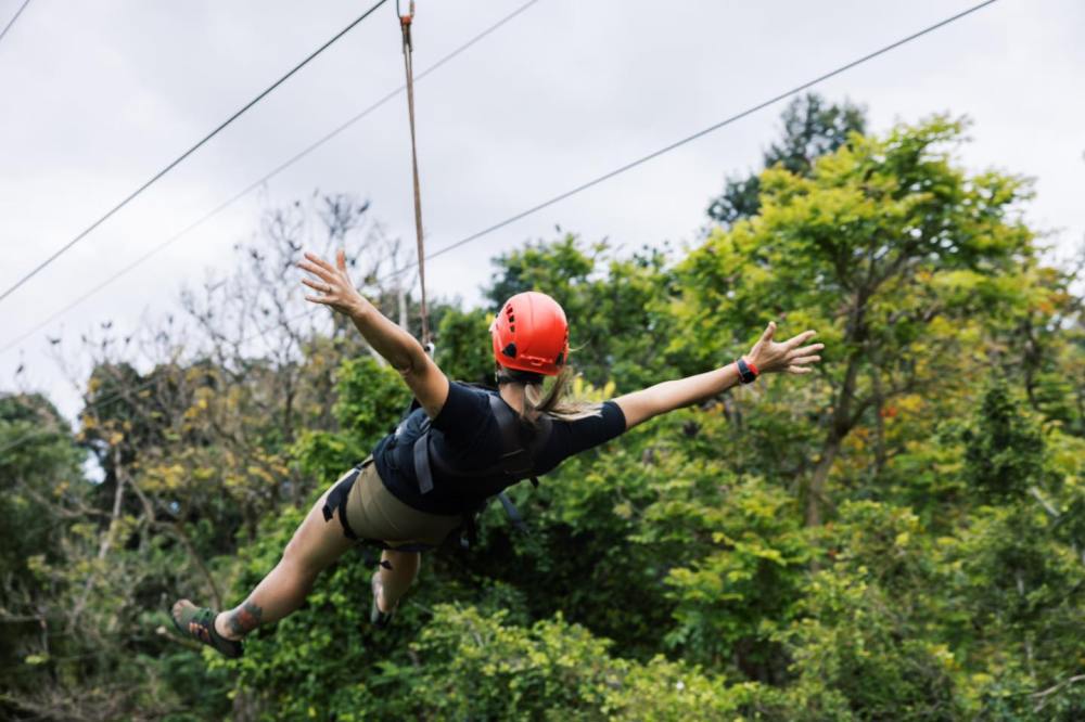 Adventure seeker soaring hands-free on one of Outfitters Kauai’s ziplines at Kipu Ranch with lush Kauai jungle views.