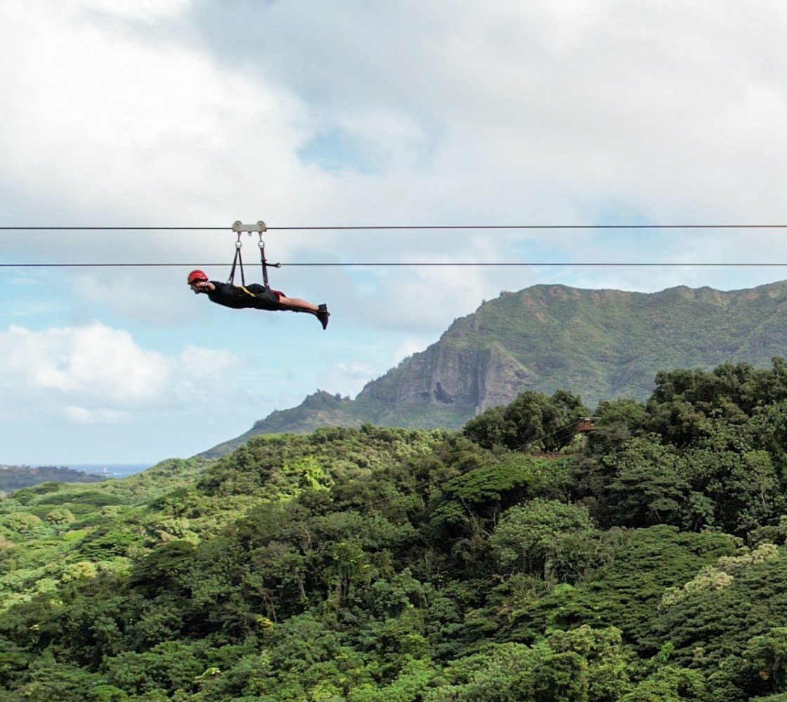 Longest zipline on Kauaʻi with rider soaring over lush green valley in Superman position