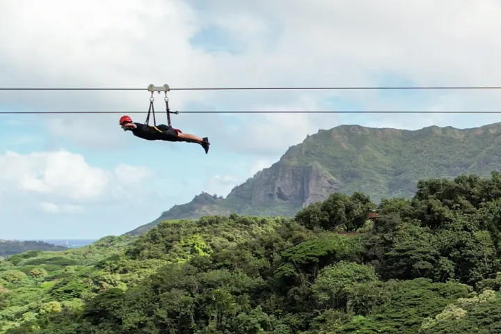 Longest zipline on Kauaʻi with rider soaring over lush green valley in Superman position