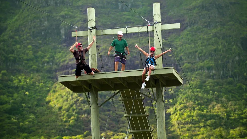 Side-by-side zipline riders flying headfirst over lush Kauaʻi landscape on the FlyLine zipline at Kīpū Ranch