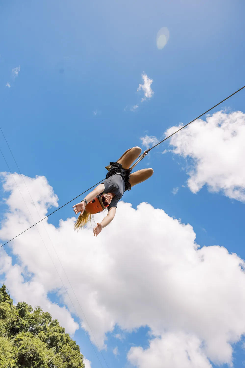 Guest riding upside down on a zipline against blue sky at Kīpū Ranch on Kauaʻi with Outfitters Kauai