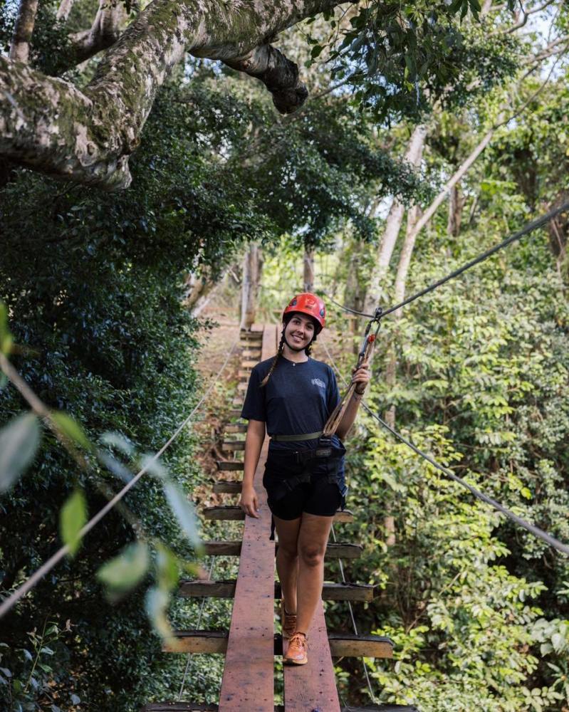 Outfitters Kauai zipline guide standing on a suspension bridge at Kipu Ranch, wearing helmet and harness surrounded by tropical forest.