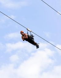 Person zip-lining through a cloudy sky, wearing safety gear and a helmet.