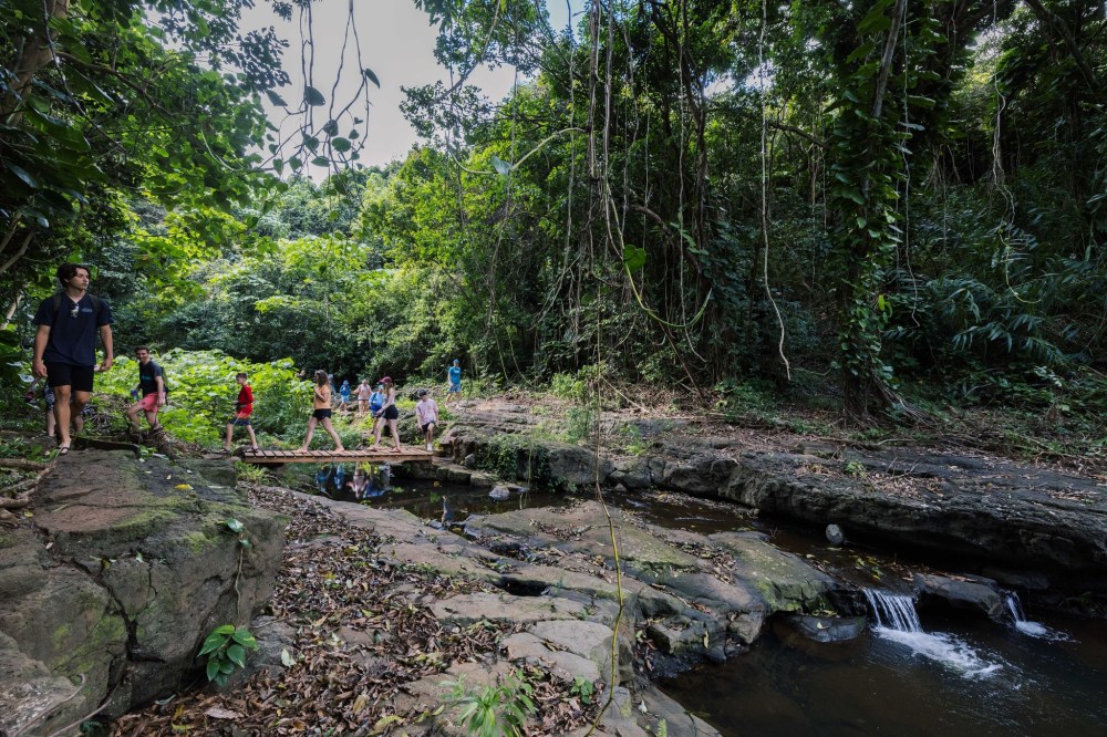 Hidden Valley Falls Kauai hiking tour with guests crossing a jungle stream bridge on a guided waterfall adventure in lush tropical rainforest